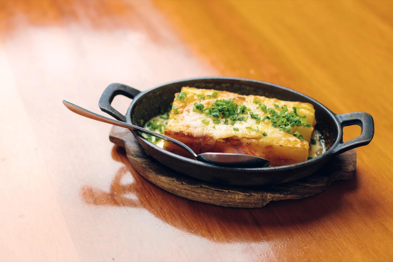 A cast-iron dish of golden potato gratin scattered with chives on a timber table
